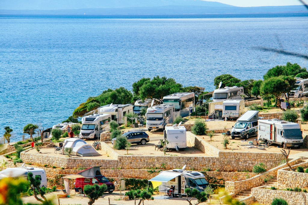 A fully occupied RV park on a sunny day with motorhomes and campers parked along a stunning blue waterfront — peak season at its best.